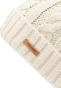 Bonnet en tricot de couleur crème, présentant des motifs texturés et un bord-côte. Comprend une étiquette en cuir marron avec le logo "VOLCOM" embossé.