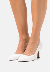 Witte pumps met hoge hak en een puntige neus, een bovenwerk van glad leer en een textuurrijke hak. Het ontwerp heeft een laag uitgesneden voorkant en een gestructureerde silhouet.