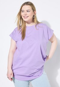 Fialové oversized tričko z měkké látky s ohrnutými krátkými rukávy, spárované s světle modrými džíny s perlami.