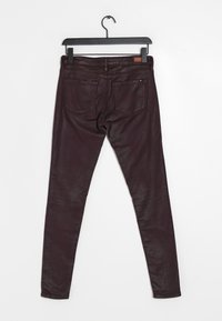 Jeans skinny bordeaux appesi a un appendiabiti, con una texture liscia, design a cinque tasche e una patch in pelle sulla vita.