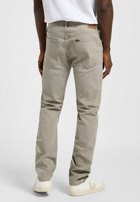 Jeans de algodón grises con ajuste slim. Cuentan con bolsillos traseros y una etiqueta de cuero con la marca en la cintura. Combinados con zapatillas de color claro.
