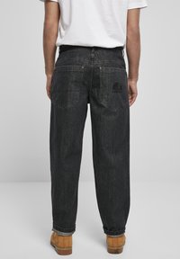 Sorte denim jeans med en afslappet pasform, der har to baglommer og et logo patch; synlige sømme og en let falmet tekstur.