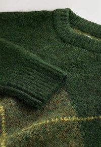 GrünerStrickpullover mit geripptem Halsausschnitt und Bündchen, aus strukturiertem Wollmaterial mit einem Patchwork-Muster in dunkleren und helleren Grüntönen sowie gelben Akzenten.