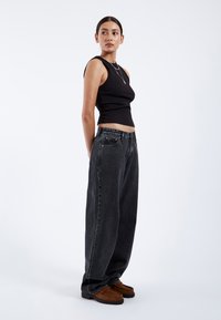 Black fitted tank top, relaxed-fit black jeans, brown slip-on shoes. Smooth fabric, wide-leg design, contrasting stitching on jeans.