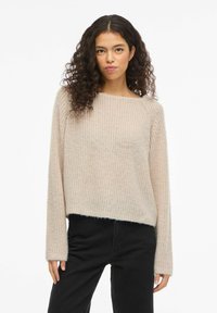 Pull en maille beige clair avec un col rond, des manches longues et une coupe décontractée. Tissu texturé avec un ourlet court et sans éléments métalliques visibles.