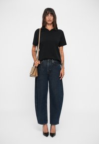 Čierna polo košeľa s krátkymi rukávmi, voľné modré džínsy a špicaté čierne lodičky. Modelka drží malú béžovú kabelku.