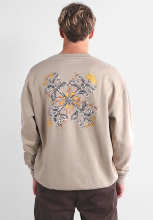 Sweatshirt beige avec un design de broderie florale en gris et jaune au dos, doté d'une coupe décontractée et de poignets côtelés.