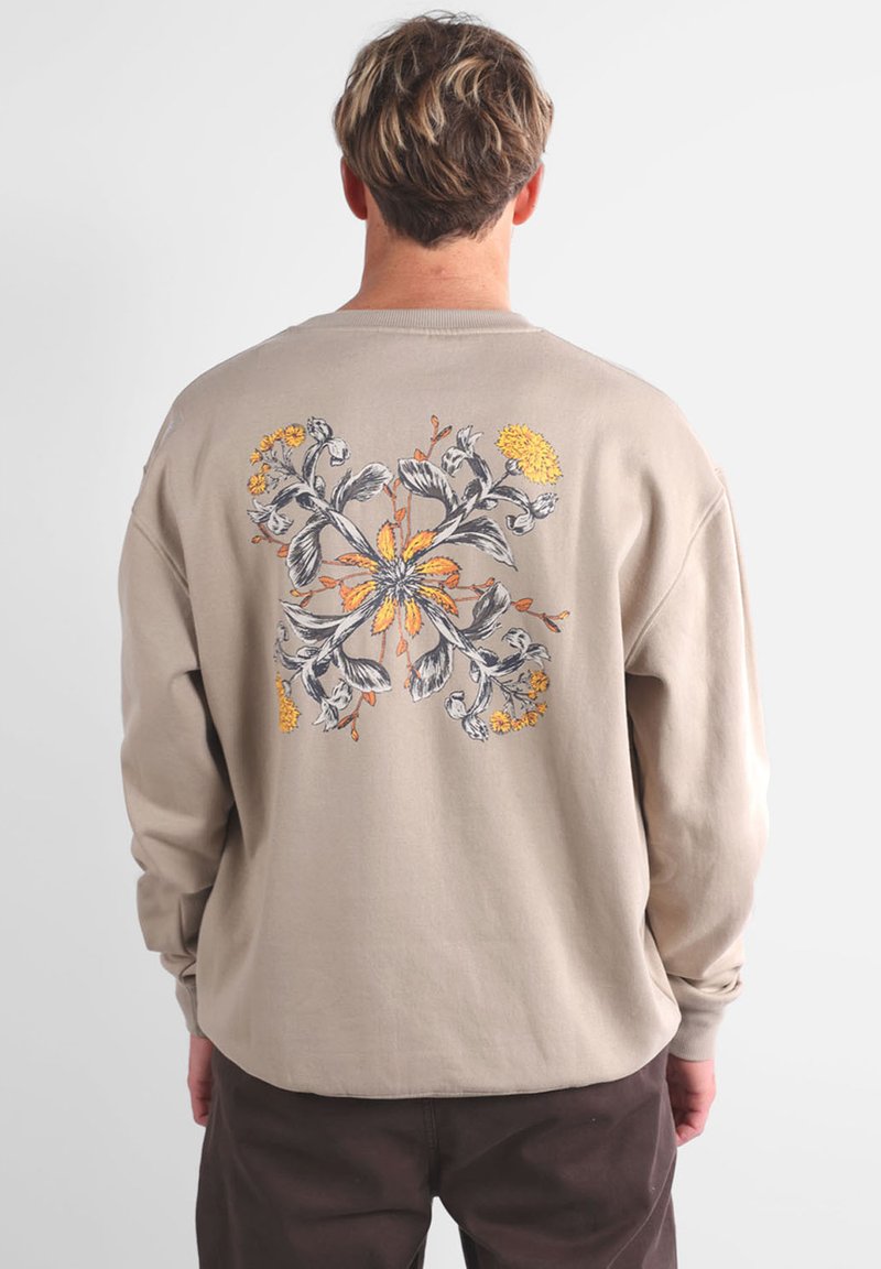 Sweat-shirt beige à manches longues, doté d'un motif floral gris et jaune au dos. Texture douce et coupe décontractée.