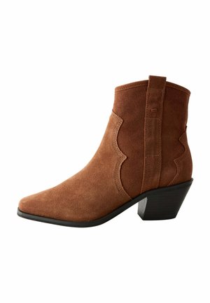 Bottine en suède marron avec un orteil pointu, des accents de design ondulé et un talon empilé. Comprend une boucle sur le dos pour l'enfiler.