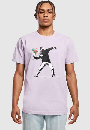 Light purple cotton t-shirt featuring a black graphic of a person throwing a bouquet of flowers with red and green accents.