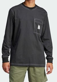 Svart långärmad skjorta med vita smala ränder, som har en framficka med etikett, rund halsringning och kontrasterande manschetter.