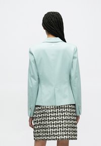 Svetlomodré priliehavé sako s hladkým povrchom, jednoklapkovým gombíkom na chrbte, skombinované s čierno-bielou vzorovanou sukňou.