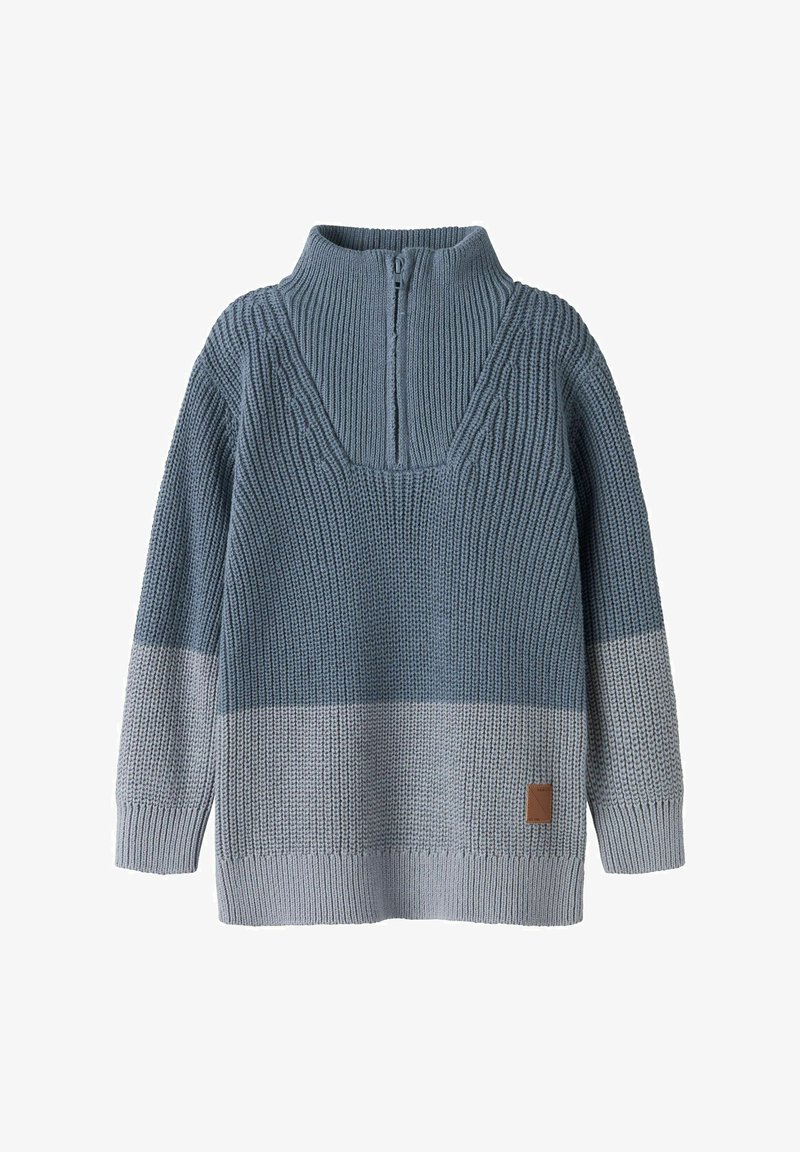 Pull tricoté bleu bicolore avec un col montant à fermeture éclair partielle et des manches longues, présentant un motif texturé et une petite pièce marron près de l'ourlet.