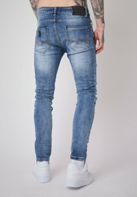 Faded blue denim skinny jeans with a slim fit, distressed details, and two back pockets, worn with white sneakers.