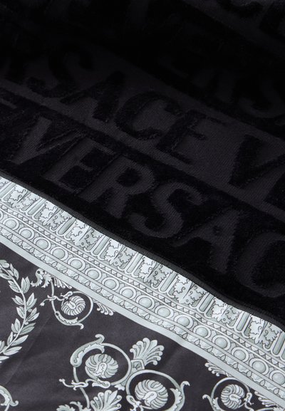 Tissu noir avec inscription "VERSACE" en relief et motif baroque décoratif blanc et gris le long du bord.