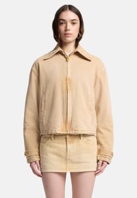 Beżowa kurtka dżinsowa z klasycznym kołnierzem, zamkiem b�łyskawicznym i opuszczonymi ramionami. Posiada przednie kieszenie i krótki krój.