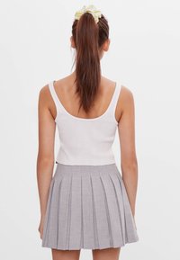 Bílý žebrovaný crop top a šedá plisovaná sukně s hladkou texturou, přiléhavým střihem a gumičkou do vlasů s mašlí.