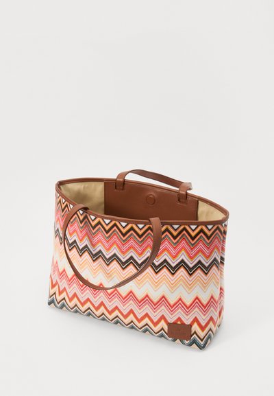 Geanta tote are un model în zigzag multicolor în nuanțe de roz, portocaliu și maro, cu mânere sintetice maro și o căptușeală interioară netedă.