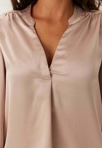 Růžová saténová blůza s výstřihem do V a sklady na ramenech, s hladkým povrchem a uvolněným střihem.