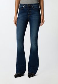 Temno modri široki jeans z visokim pasom, narejeni iz денима. Imajo kontrastno šivanje in sprednje žepke. V kombinaciji z črnimi čevlji s koničastim nosom.