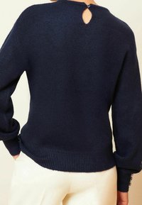 Pull en maille bleu marine à texture douce, manches oversize, poignets et ourlet côtelés, avec une ouverture en forme de goutte d'eau au dos fermée par un bouton.