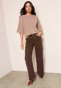 Smėlinis megztinis su apvaliu kaklu ir plačiomis rankovėmis, derinamas su rudiems tiesiais kelnėmis ir rudais smailiais bateliais.