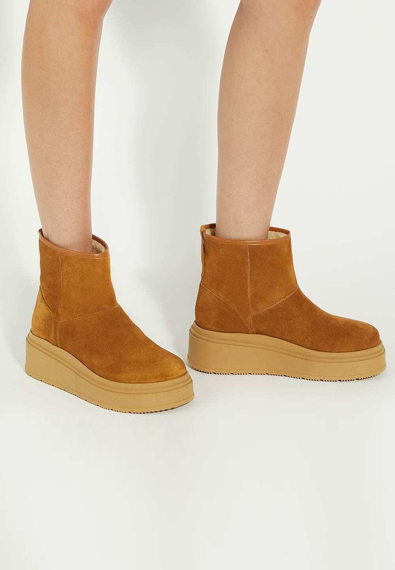 Bruine suède enkelboots met een platte, lichtbeige plateauzool. Heeft een afgeronde neus en een eenvoudig ontwerp zonder versieringen.
