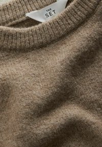 Beżowy dziergany sweter z prążkowanym okrągłym dekoltem i białą metką z napisem THE SET wsuniętą wewnątrz kołnierza.