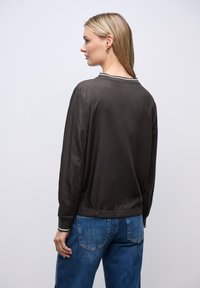 Giacca di raso verde scuro con una vestibilità ampia, polsini e orlo a coste. Presenta un colletto a contrasto ed è abbinata a jeans blu.