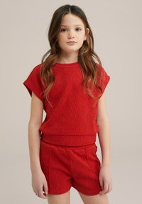 Piros textúrájú, két részes szett, amely rövidujjú felsőből és lazán szabott, passzoló sortból áll, kiemelve az összhangzó dizájnt.