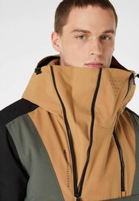 Herrenjacke mit hohem Kragen, Reißverschluss und einem Farbblockdesign in Braun, Grün und Schwarz. Der Stoff hat eine glatte Textur mit perforierten Details.