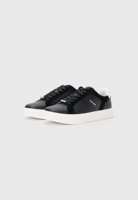 Zwarte sneakers met een gladde leren bovenkant, witte rubberen zool, vetersluiting en subtiele merkdetails aan de zijkant.