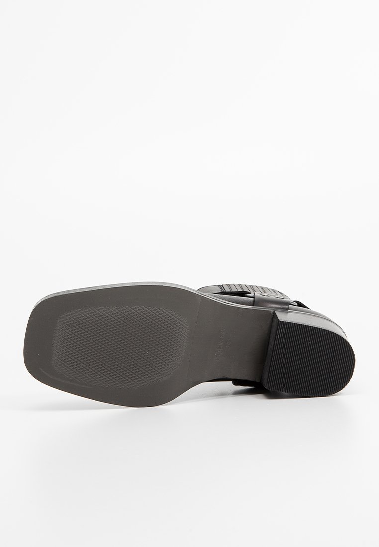 Suola di scarpa nera con un motivo di grip testurizzato, bordi lisci e un leggero tacco rialzato. Presenta un design elegante e materiale resistente.