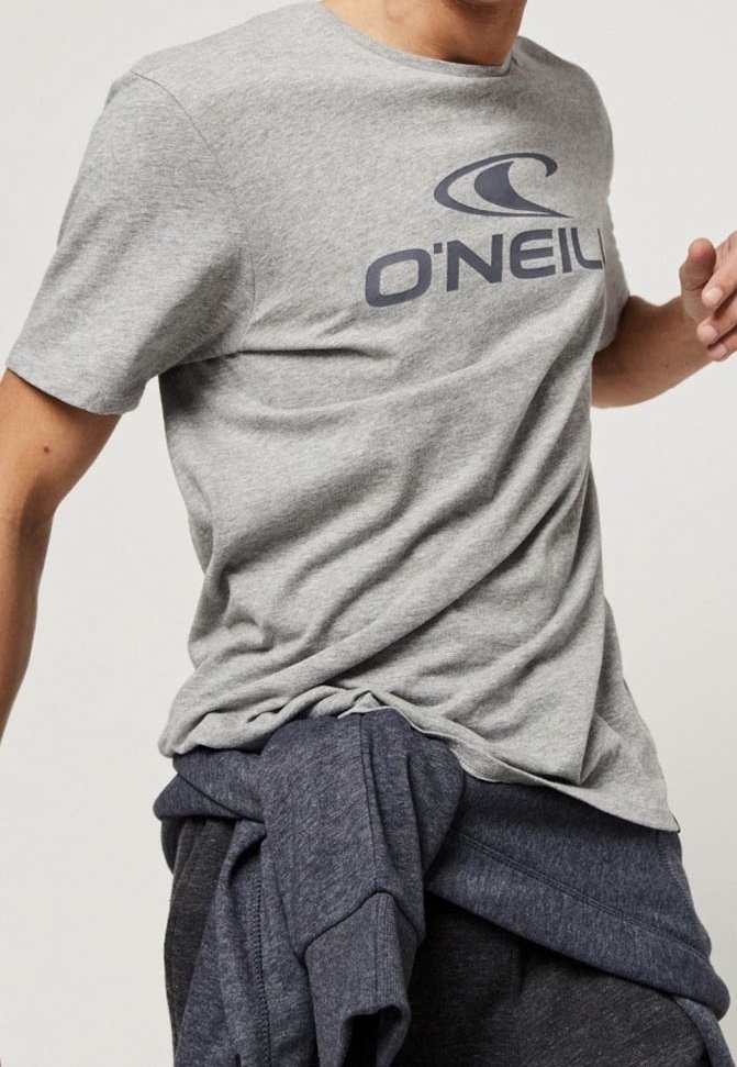 T-shirt gris à manches courtes avec un logo "O'NEILL" bleu foncé sur la poitrine. Tissu doux et coupe décontractée. Superposé avec un sweat bleu marine à la taille.