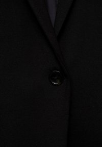 Black blazer featuring a smooth fabric, structured lapels, and a shiny black button. Simple design with no additional patterns or accents.