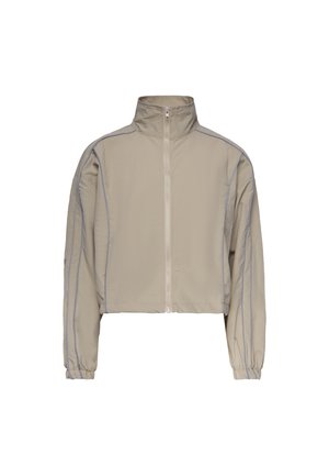 Giacca beige corta con collo alto, cerniera frontale, maniche lunghe e cuciture blu visibili lungo le braccia e le spalle.