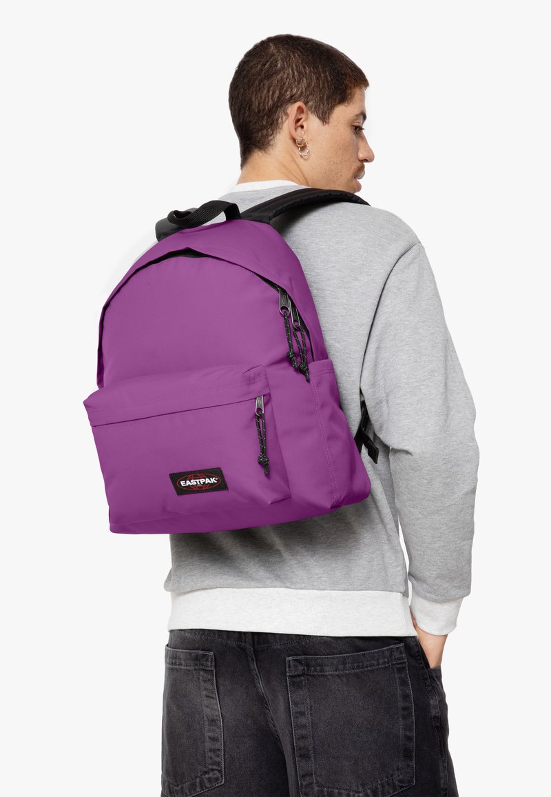 Mochila morada con un gran compartimento principal, bolsillo frontal y detalles en cremallera negra. Hecha de tela duradera, cuenta con correas de hombro ajustables.