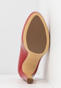 Rød læder højhælet sko med spids tå. Glat overflade med en struktureret brun sål og en let tilspidset hæl. Størrelse 37.