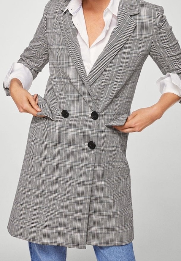 Blazer doppiopetto grigio a quadri con bottoni neri, revers a punta e tasche laterali. Tessuto liscio con vestibilità sartoriale.