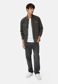 Mørkegrå knap-op kordfløjl skjorte med to brystlommer, båret over en hvid t-shirt. Parret med mørke jeans og hvide sneakers.