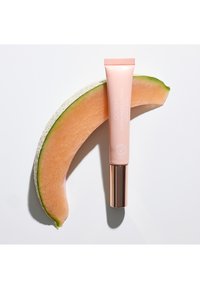 Un tubo di balsamo labbra colorato GOSH rosa con SPF15 appoggiato su una fetta di melone cantalupo arancione su uno sfondo bianco.