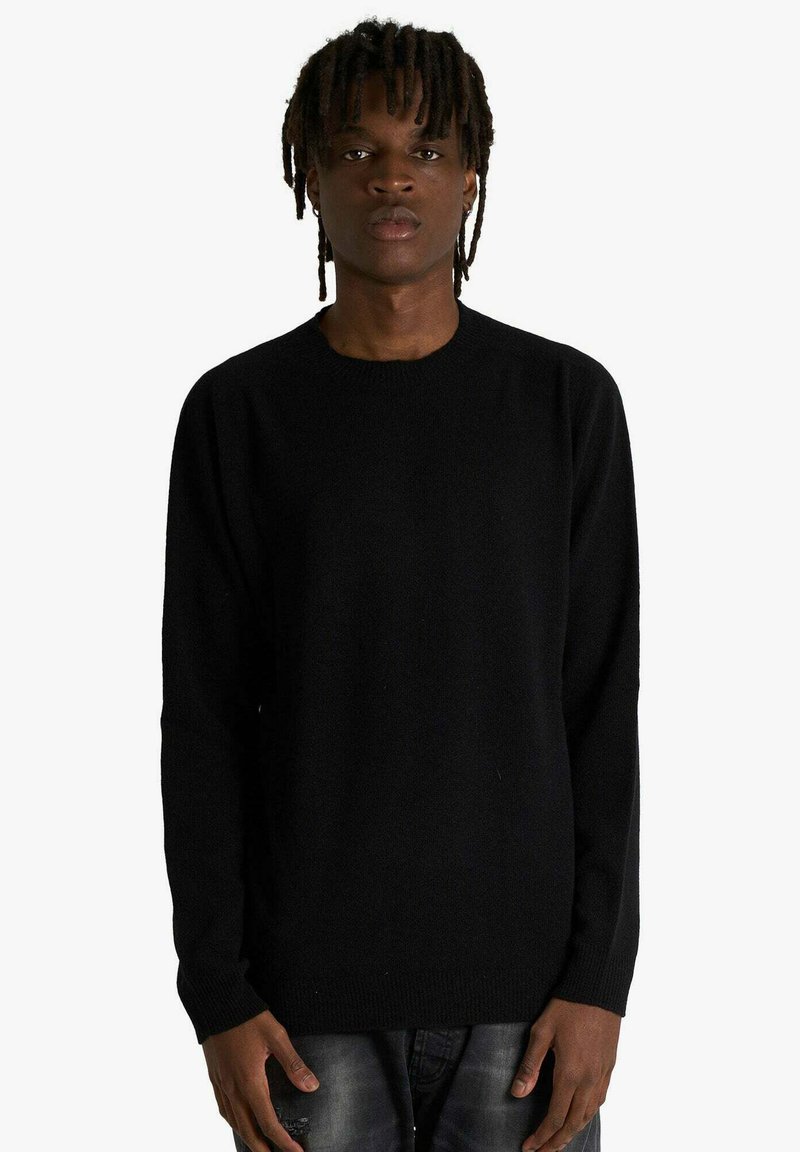 Maglione nero lavorato a maglia con scollo rotondo e maniche lunghe, caratterizzato da una texture morbida e una vestibilità classica. Indossato con jeans strappati.