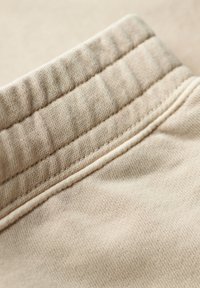 Beige stof met een gemêleerde elastische tailleband. Zichtbare stikdetails en een gladde textuur. Close-upweergave benadrukt de zachtheid en flexibiliteit.