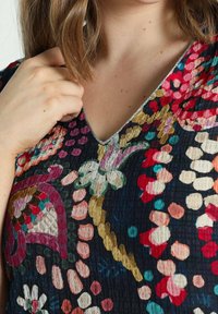Top con estampado que presenta un escote en V en tejido oscuro con diseños florales y de puntos coloridos; superficie texturizada y sutil ribete metálico a lo largo del escote.