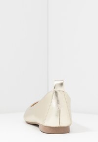 Kultainen metallinen ballerina, jossa on terävä takaosa, sileä pinta, minimalistinen muotoilu ja pieni korko. Sopii eri tilaisuuksiin.