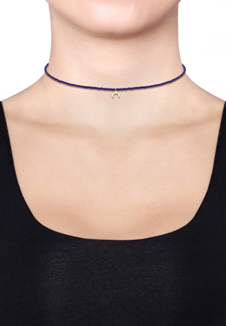 Blå flettet choker-nedhalskæde med en lille guld halvmånecharme i midten. Glat tekstur, enkelt design.