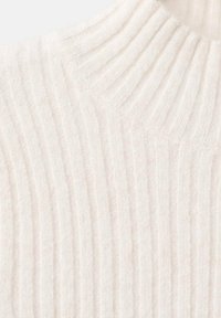 Suéter de punto color crema con cuello alto acanalado, que presenta una textura vertical y un material suave y peludo.