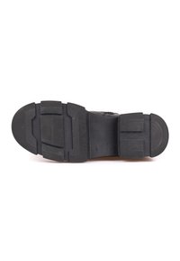 Suela de zapato de goma negra con un patrón texturizado, que presenta un tacón ancho y un diseño de surcos segmentados para una mejor adherencia y durabilidad.