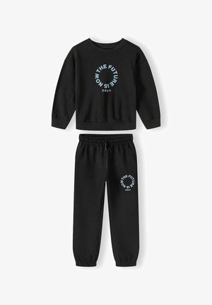 Ensemble sweat-shirt noir et joggings avec texte circulaire bleu clair « THE FUTURE IS NOW » et petits caractères japonais sur les deux pièces.