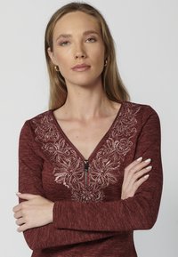 Burgundská mikina s dlhým rukávom na zips, so vzorom kvetov pozdĺž výstrihu a štruktúrovanou tkaninou.